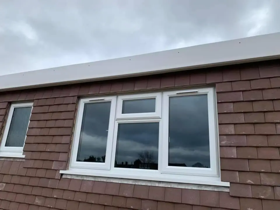 A finished dormer face with hanging tiles and new white windows