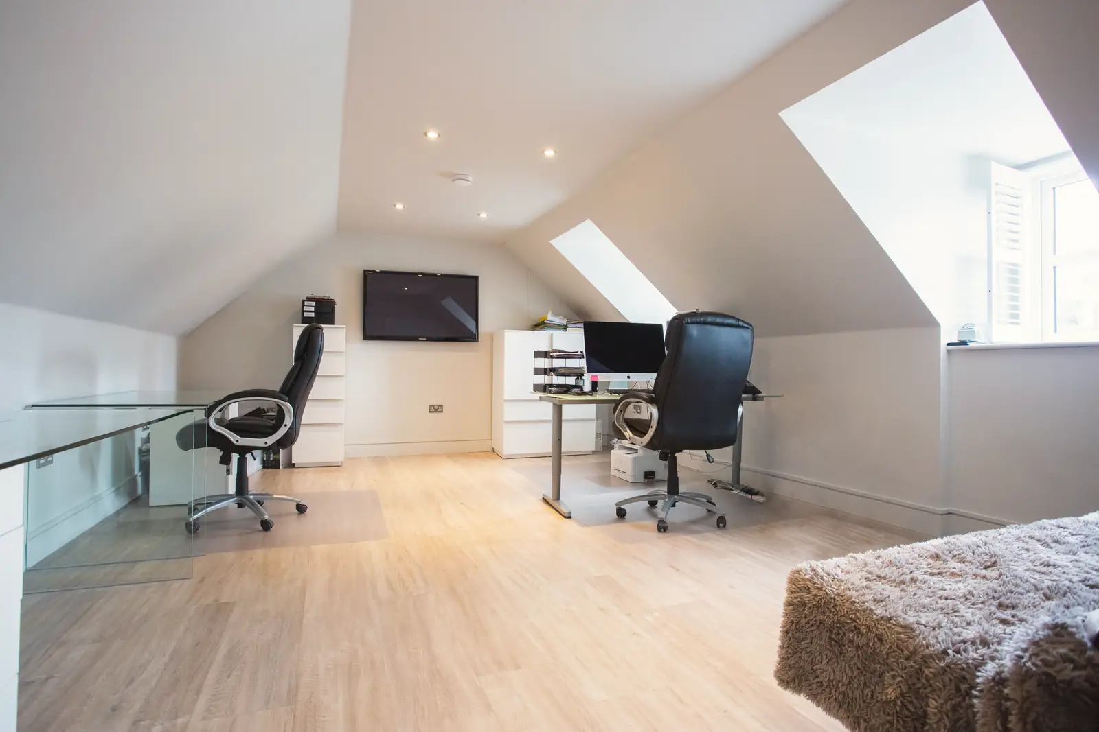 A finished loft room with a large dormer window, a roof window, downlights and a desk area